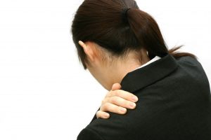 明石市 肩こり でデスクワーク中に肩の重だるさを感じるスーツ姿の女性